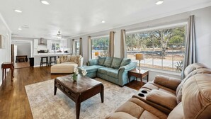 A spacious living room with a sectional sofa, a coffee table, and a view of the outdoors through large windows. - Wonder World Retreat (San Marcos)
