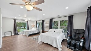 A spacious bedroom with two beds, a massage chair, a ceiling fan, and large windows with curtains. - Wonder World Retreat (San Marcos)