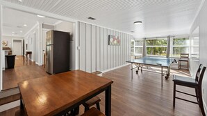 A spacious kitchen with a wooden table and chairs, a large window with blinds, and a refrigerator. - Wonder World Retreat (San Marcos)