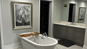 Ein modernes Badezimmer mit einer freistehenden Badewanne, einem großen Spiegel und einem gerahmten Bild an der Wand.