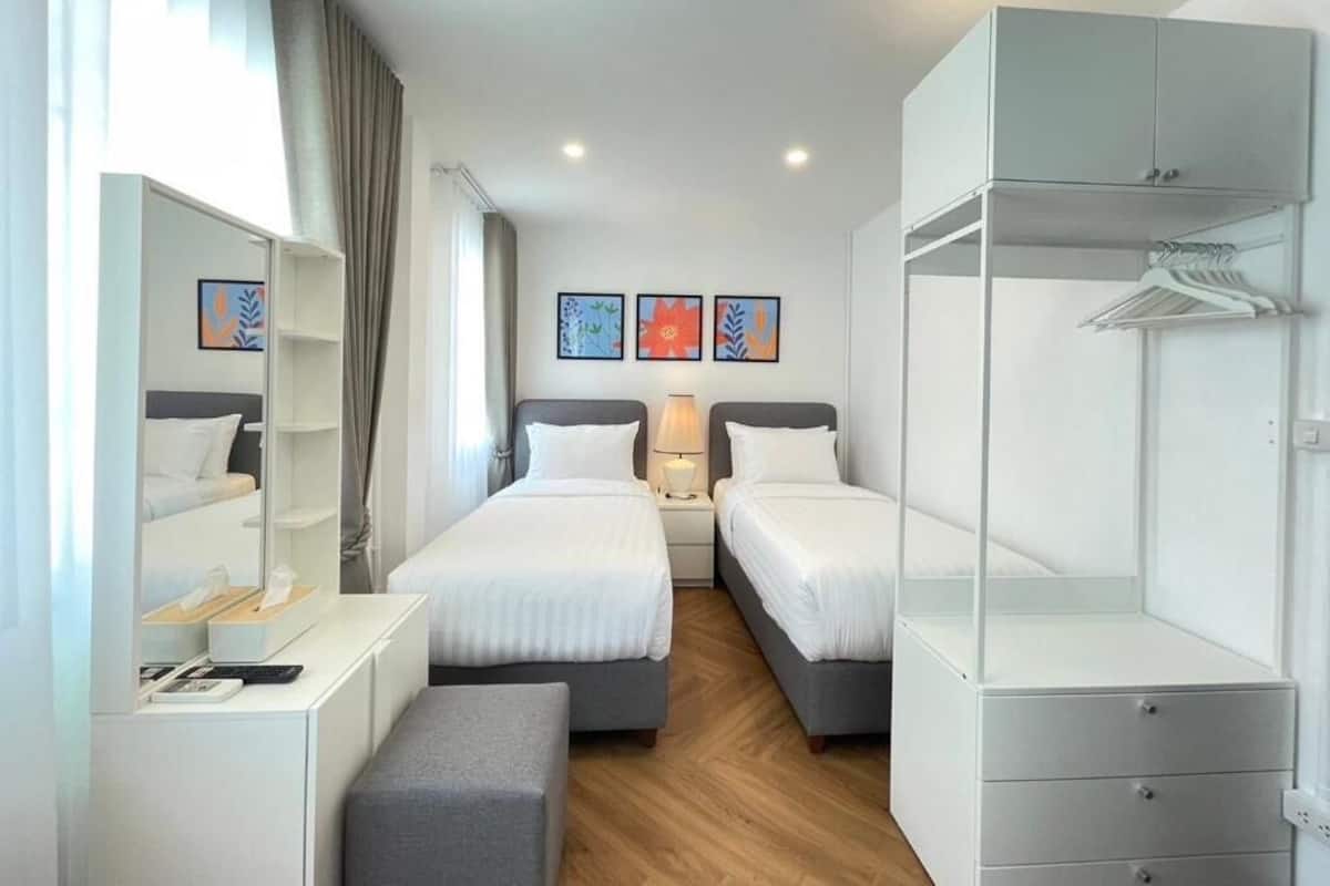 A modern hotel room with two beds, a wardrobe, a desk, and a mirror.