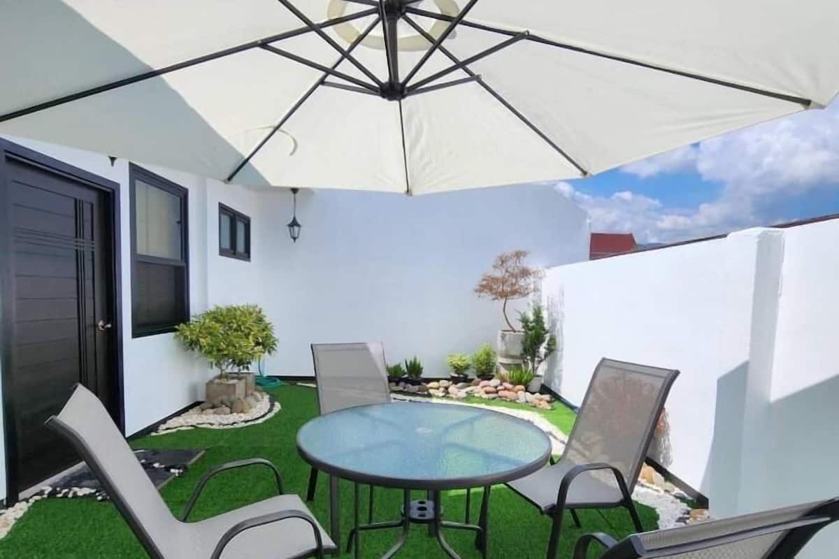 A patio with a round glass table and four chairs, surrounded by artificial grass and potted plants.