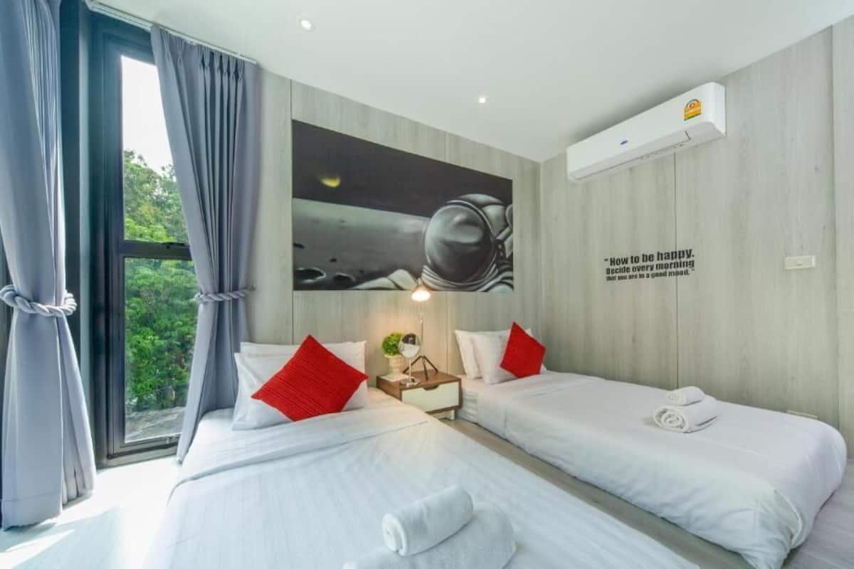 A hotel room with two beds, a large window with curtains, a wall-mounted air conditioner, and a motivational quote.