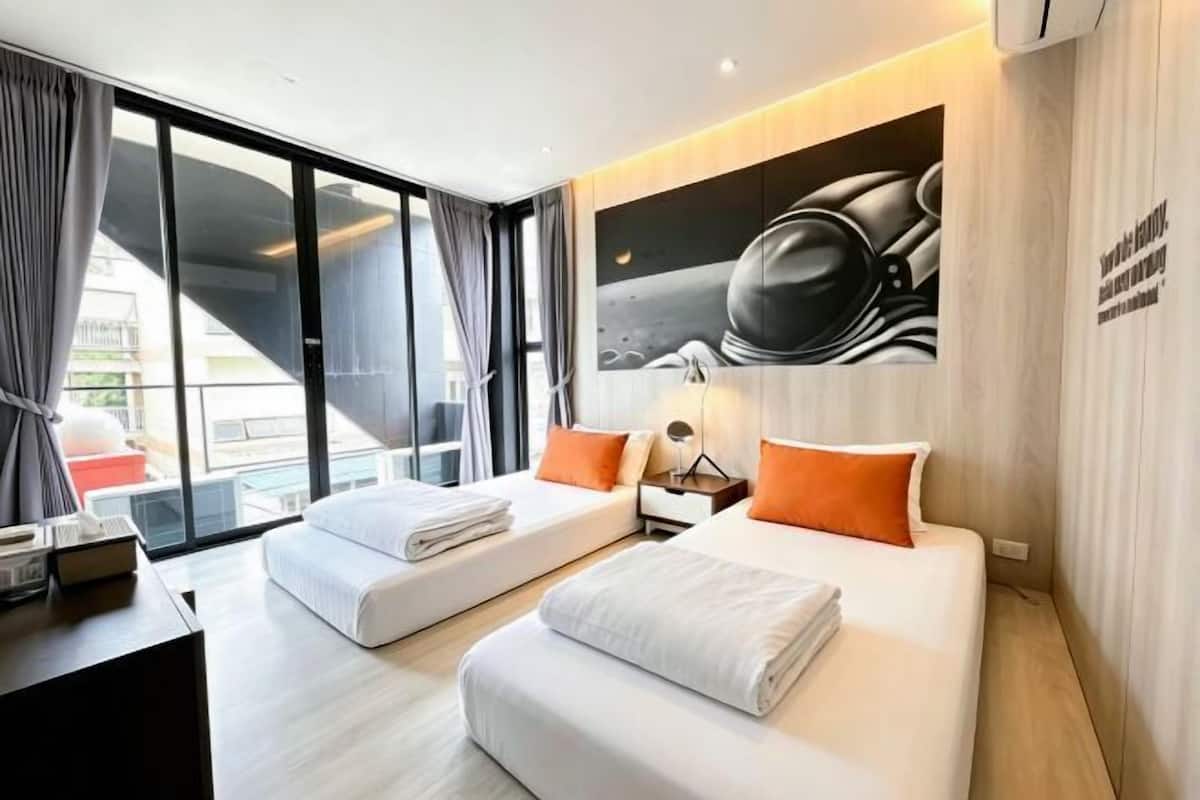 A modern hotel room with two beds, a large window, and a wall-mounted artwork.