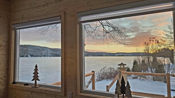 Una habitación con dos ventanas amplias que dan vistas a un lago helado y colinas circundantes.