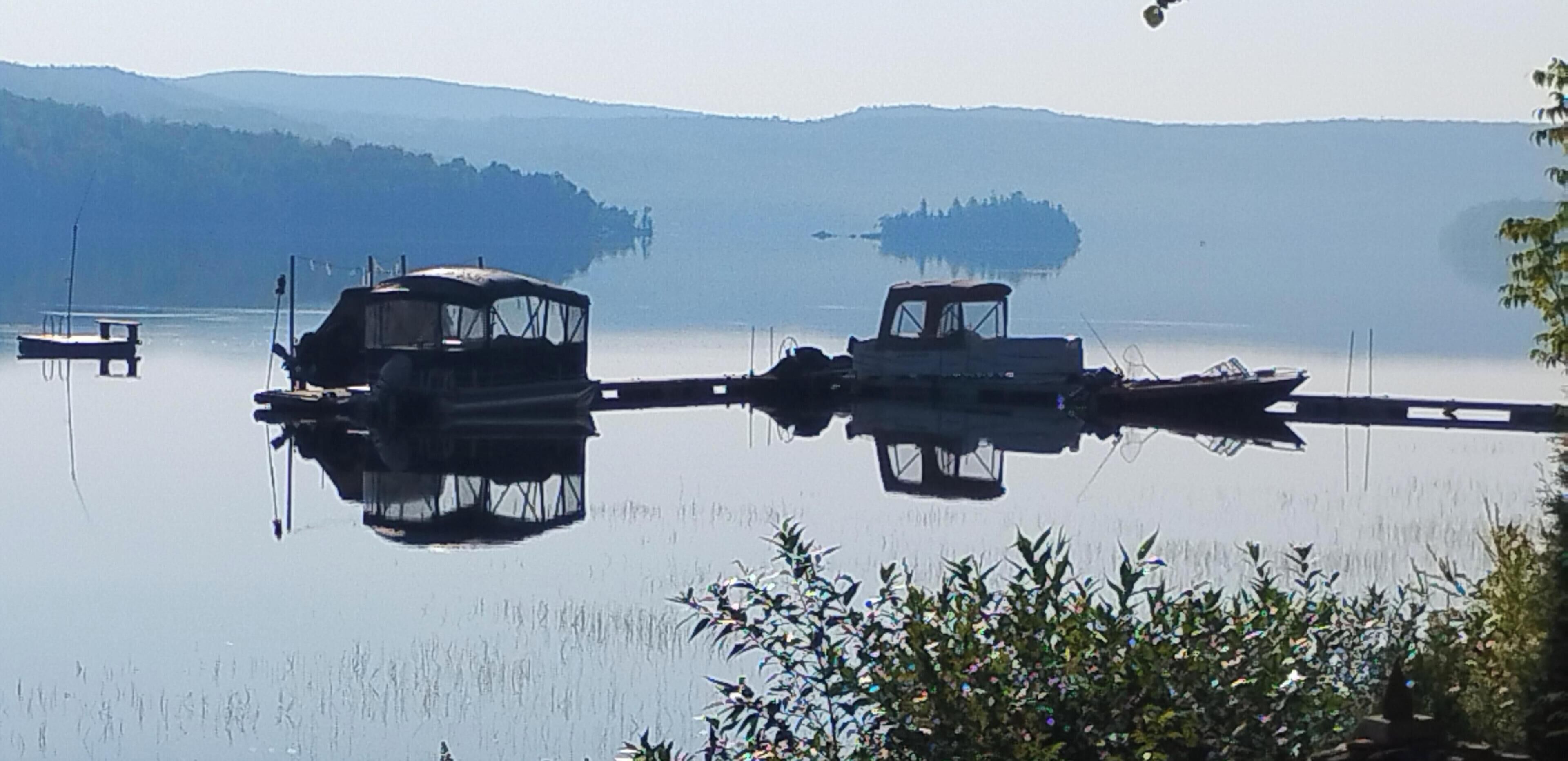 Un lago tranquilo con dos barcos amarrados a la orilla, rodeado de colinas y vegetación.