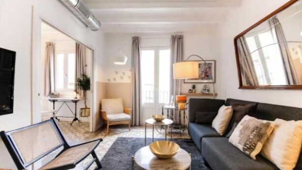 A modern living room with a sofa, armchair, and coffee table. There is a large mirror on the wall and a window with curtains. - Boutique Living in the Heart of Barcelona (Barcelona)