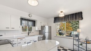 A modern kitchen with white cabinets, a stainless steel refrigerator, a checkered floor, and a window with a view of trees.