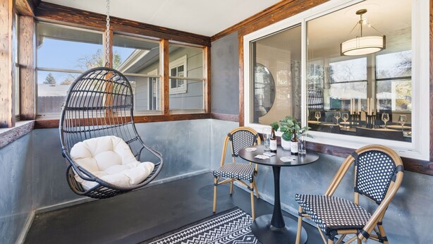 A cozy outdoor seating area with a hanging chair, two chairs, and a table with drinks.