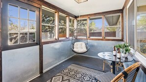 A sunroom with large windows, a hanging chair, a table with chairs, and a small potted plant.