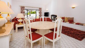 Un coin repas avec une table ronde et des chaises, un canapé avec des coussins rouges, un téléviseur et une cheminée.