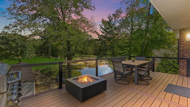 A deck with a fire pit, outdoor seating, and a view of a pond and trees.