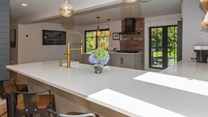 A modern kitchen with a large island, pendant lighting, and a view of the outdoors.