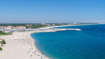 Una playa con agua azul cristalina, orilla de arena y edificios al fondo.