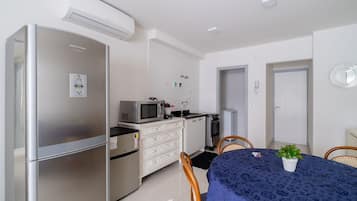 Una cocina compacta equipada con refrigerador, microondas y estufa. Hay una mesa de comedor con sillas y una planta en maceta.