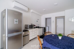A compact kitchen with a refrigerator, microwave, and stove. There is a dining table with chairs and a potted plant. - Apartments 110 m From the Beach in Floripa - AGC (Florianópolis)