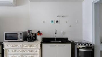 Una cocina compacta con un refrigerador blanco, un microondas, una estufa y un armario blanco con cajones.