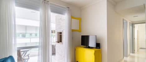 A modern living room with a blue sofa, a yellow cabinet with a TV, and a large window with curtains.