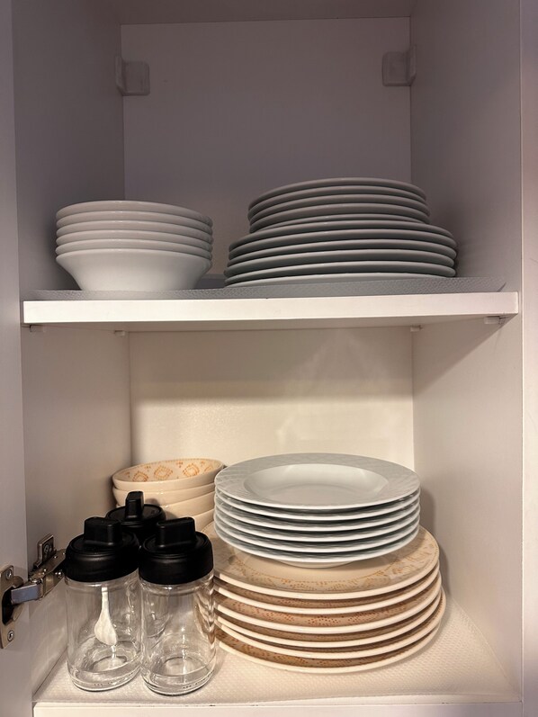 Un mueble de cocina con estantes blancos que contienen pilas de platos y cuencos.