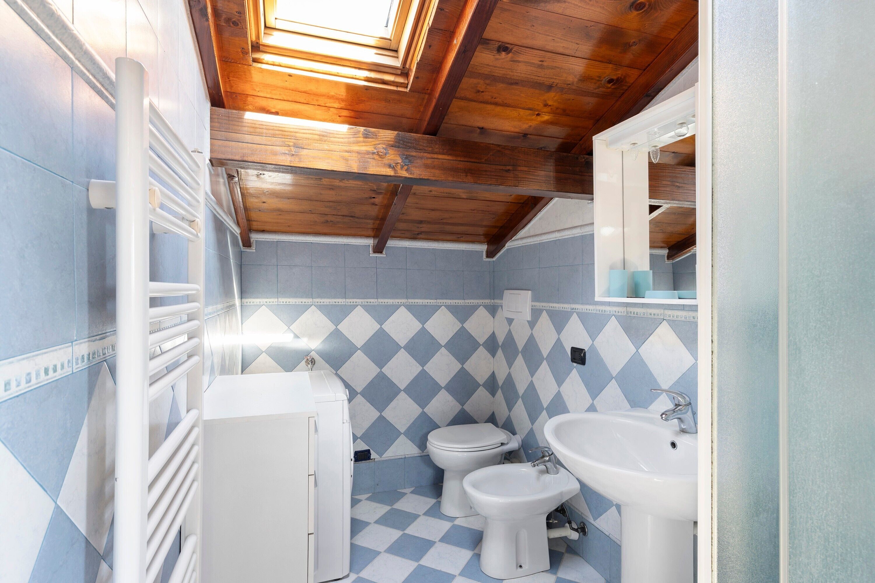 Un bagno con pavimento a scacchi, un water, un bidet, un lavandino e un portasciugamani.