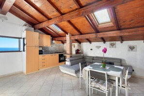 Una cocina con horno integrado, una zona de comedor con mesa y sillas, un sofá gris y un tragaluz.