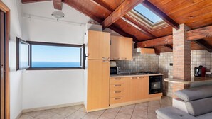 Een keuken met houten kastjes, een fornuis en uitzicht op de zee door een raam.