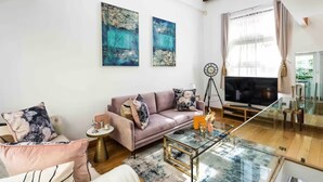 Ein modernes Wohnzimmer mit einem rosa Sofa, einem Glastisch und abstrakter Kunst an der Wand.