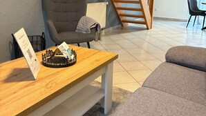 A modern living room with a wooden bench, a grey sofa, a black chair, and a wooden staircase. - Vacation apartment Aischgrund - 75 m² | near Nuremberg, Bamberg & Steigerwald (Lonnerstadt)