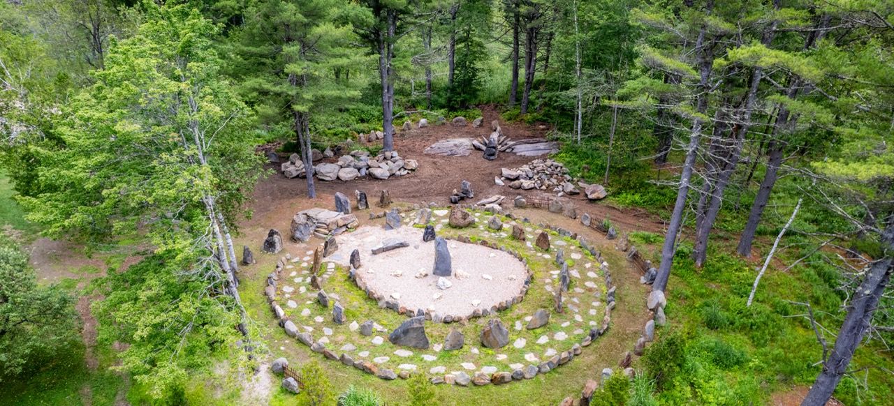 A circular stone arrangement in a forested area with trees and greenery around.