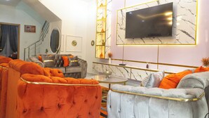 A modern living room with a sofa set, a television mounted on a marble wall, and a staircase leading to another level. - Fortified 4 Bedroom Home (Lekki)
