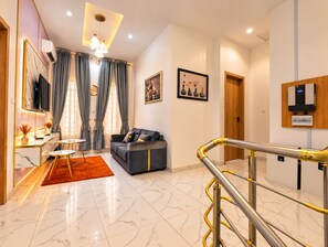 A modern living room with a sofa, a coffee table, and a TV. There is a staircase with a handrail leading to another level. - Fortified 4 Bedroom Home (Lekki)