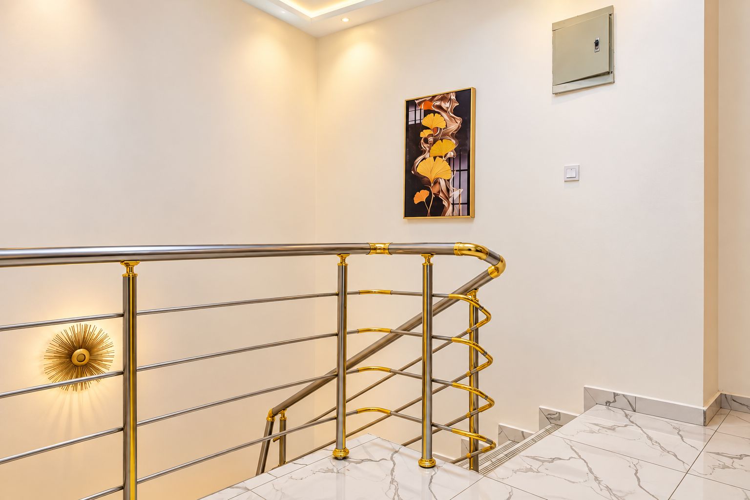 A modern interior with a metal staircase railing, a wall-mounted light fixture, and a framed artwork.