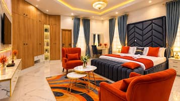 A modern hotel room with a large bed, a sitting area with a sofa and armchairs, a desk, and a television.