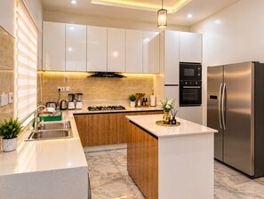 A modern kitchen with white cabinets, a stainless steel refrigerator, a gas stove, and a central island with a vase of flowers.