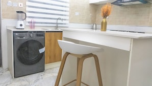 A compact kitchen with a washing machine, a sink, and a bar stool. - Fortified 4 Bedroom Home (Lekki)