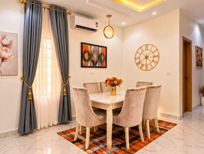 A dining area with a marble table, cushioned chairs, a patterned rug, and a wall clock. - Fortified 4 Bedroom Home (Lekki)