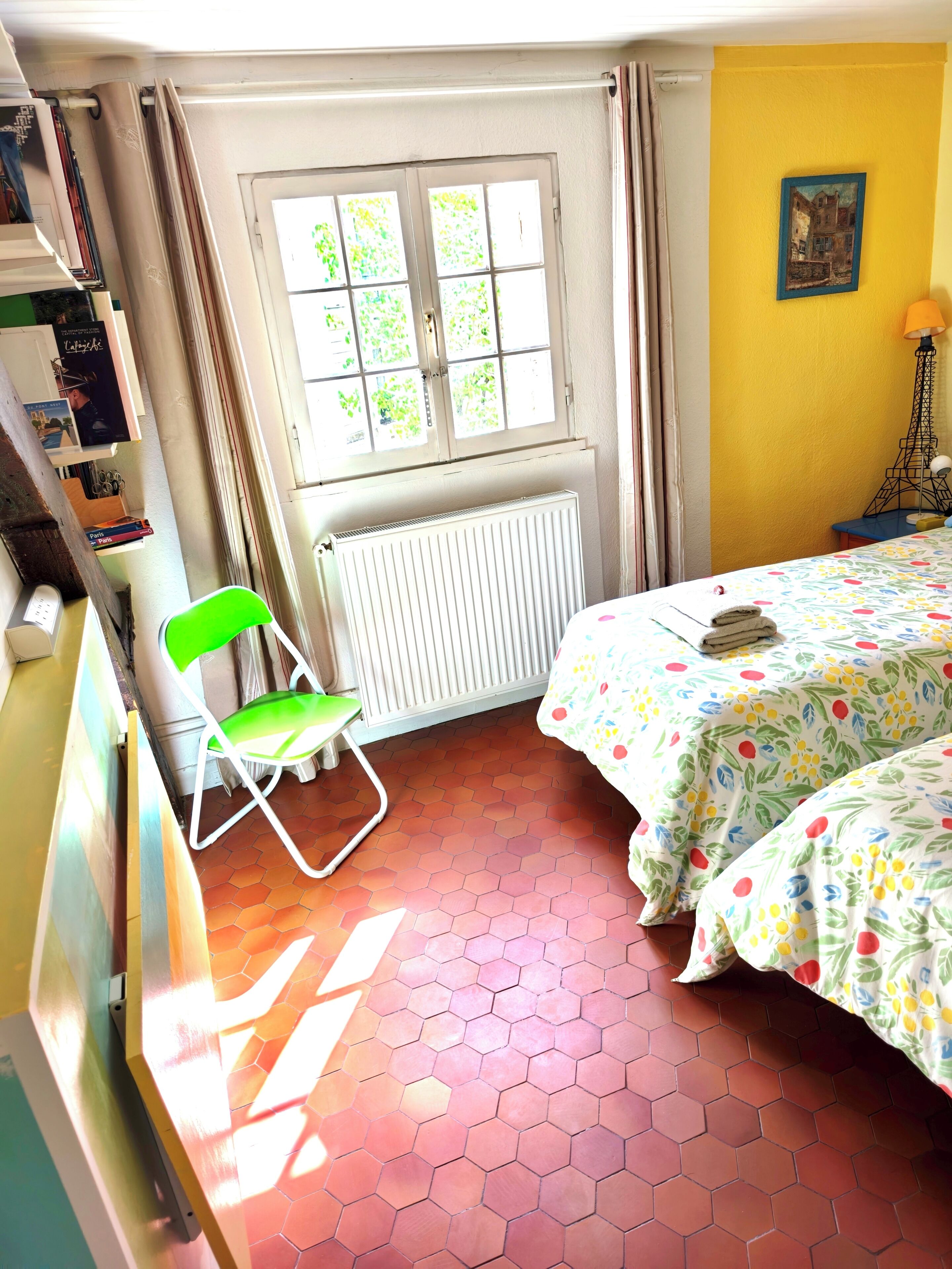 Une pièce comprenant un lit, un radiateur, une fenêtre avec des rideaux, une chaise et une bibliothèque.