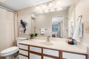 Une salle de bain moderne avec un grand miroir, un lavabo et des toilettes. On peut voir des plantes sur le comptoir et des serviettes accrochées au mur.