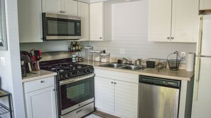 Une cuisine avec des meubles blancs, une cuisinière en acier inoxydable, un four à micro-ondes, un lave-vaisselle et un évier.