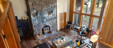 A cozy living room with a stone fireplace, leather sofa, and a large window offering a view of the outdoors.