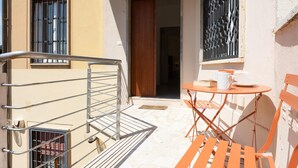A small outdoor seating area with a table and chairs, a metal railing, and a door leading to an interior space. - Rental in Rome Vatican Secret Apartment (Rome)