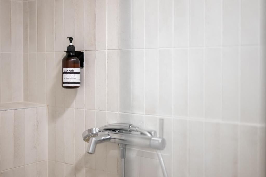 Ein Badezimmer mit weißen Fliesen, einer Duschbrause und einer Körperpflegeflasche.