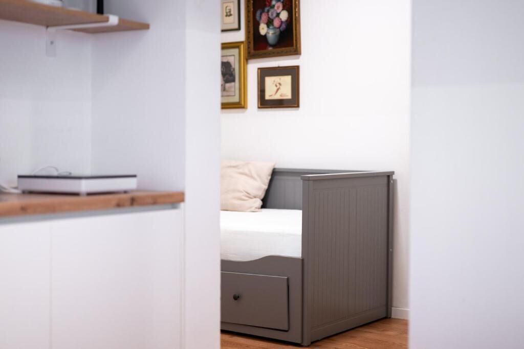 Un dormitorio con una cama, una mesita de noche, un cajón y una estantería con un dispositivo.