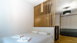A modern hotel room with a wooden slatted headboard, a bed with white linens, and a grey sofa. - The Vlasta Collection (Zagreb)