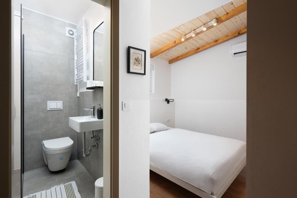 Une salle de bain avec des toilettes, un lavabo et une douche, et une chambre avec un lit et un plafond en bois.