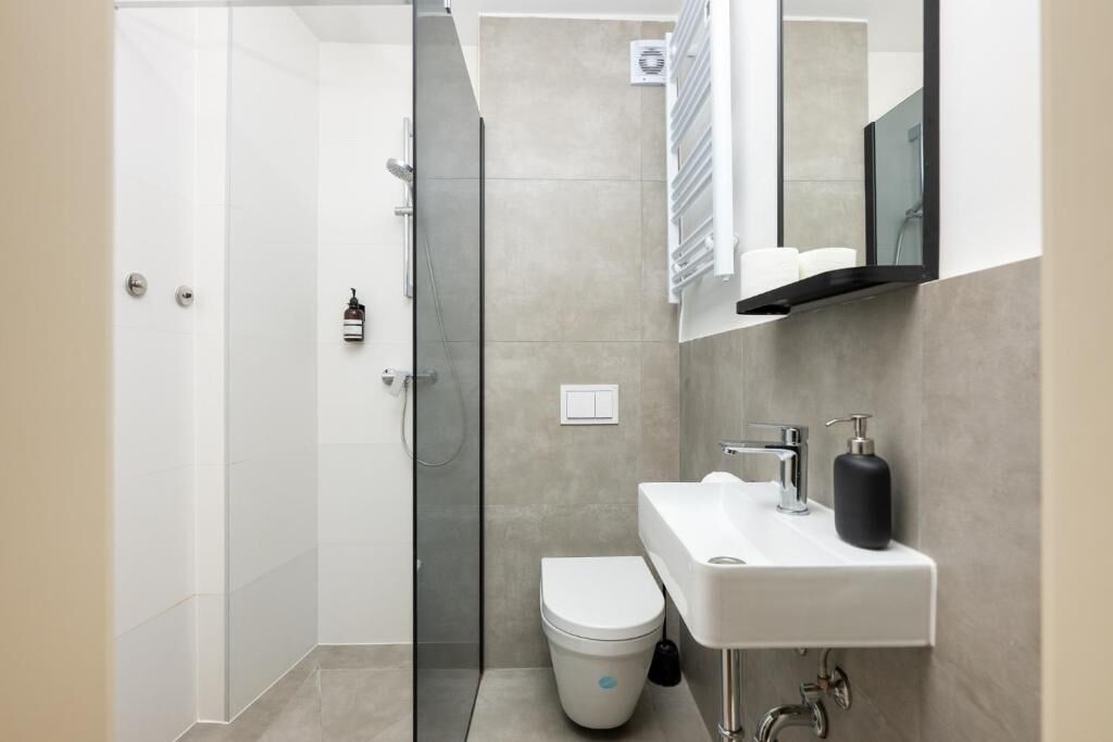 A modern bathroom with a glass shower enclosure, a white toilet, a sink with a mirror above, and a towel rack.