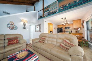 A living room with a sofa and armchairs, a dining area with a table, and a kitchen with wooden cabinets.