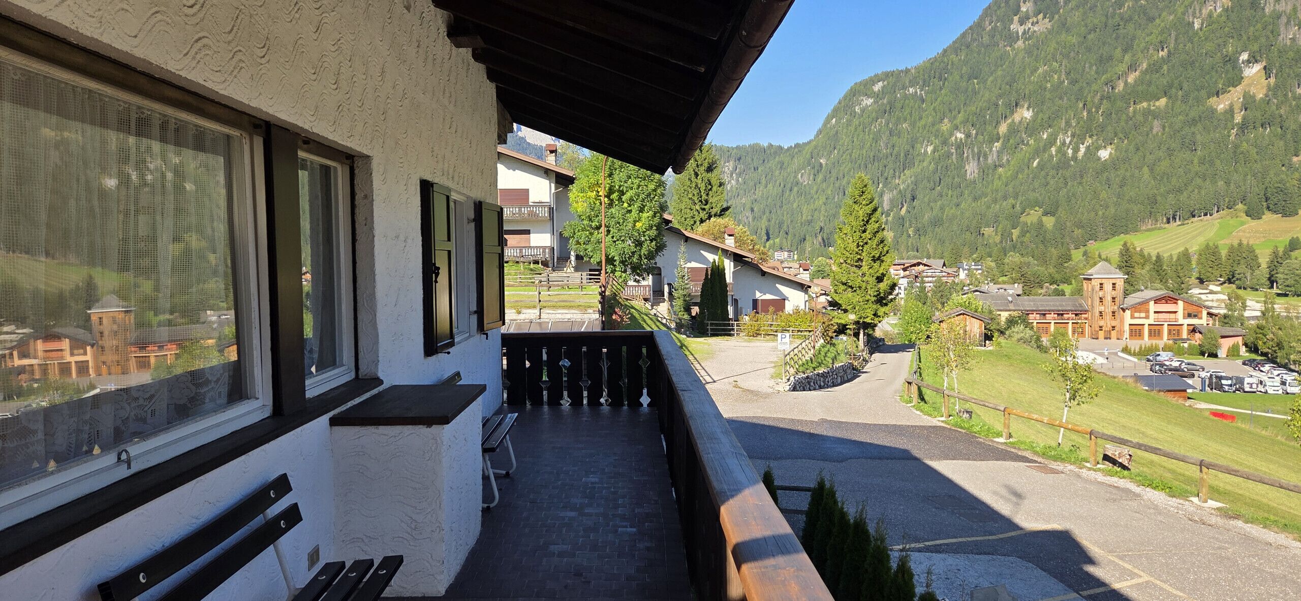 Un balcon avec vue sur un village de montagne, des bancs et un espace de stationnement.