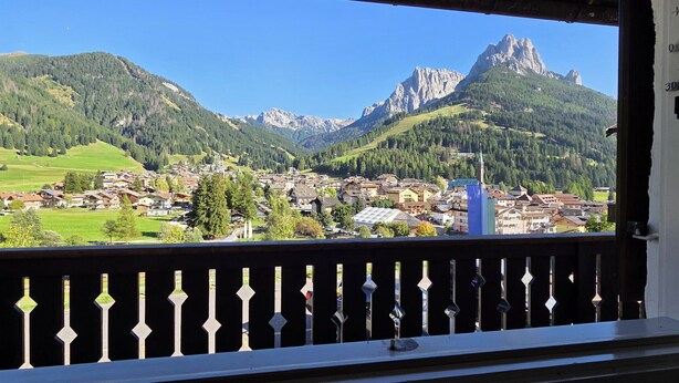 A balcony with a view of a town nestled in a valley, surrounded by mountains. - House Scacciapensieri (Pozza di Fassa)