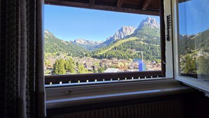 A window view of a mountain village with a prominent peak, a church spire, and a small town below. - House Scacciapensieri (Pozza di Fassa)